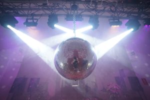 Bola de discoteca grande colgada de un puente de iluminación e iliminada con focos beam